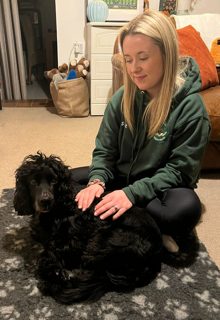 Jo kneeling on a rug at home, gently massaging a black spaniel